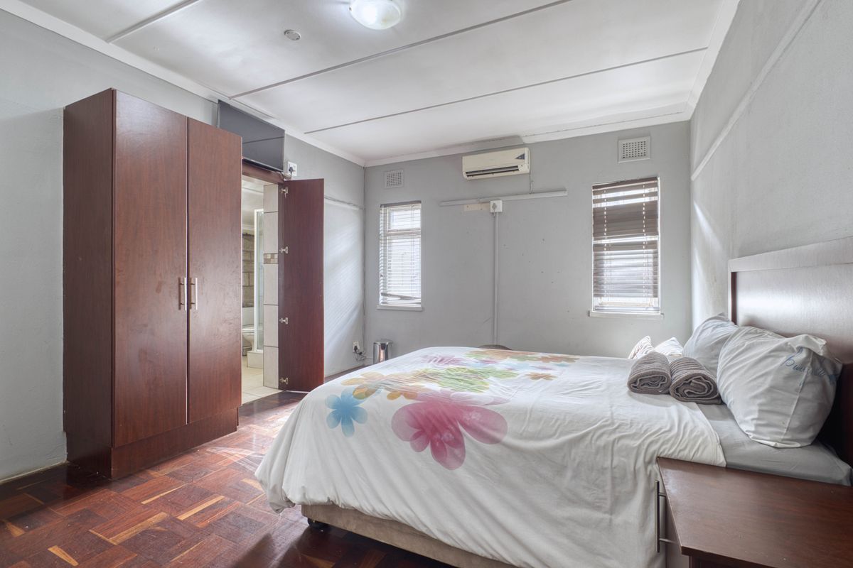 A bedroom featuring parquet flooring, a built-in wardrobe, split-system air conditioning, and an en-suite bathroom.