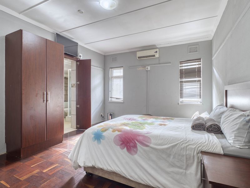 A bedroom featuring parquet flooring, a built-in wardrobe, split-system air conditioning, and an en-suite bathroom.