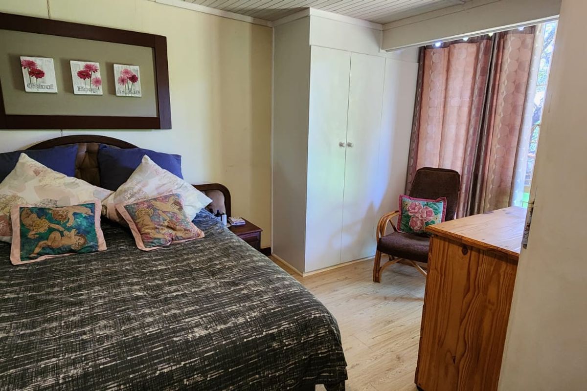 A functional bedroom featuring built-in cupboards, light wood-look flooring, and a window with curtain treatments.