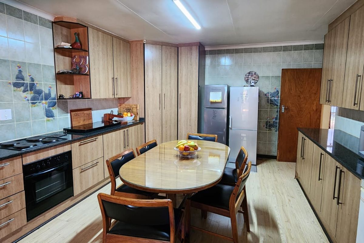 A functional kitchen featuring wood-look cabinetry, dark granite countertops, built-in oven, and hob, with an integrated dining area.