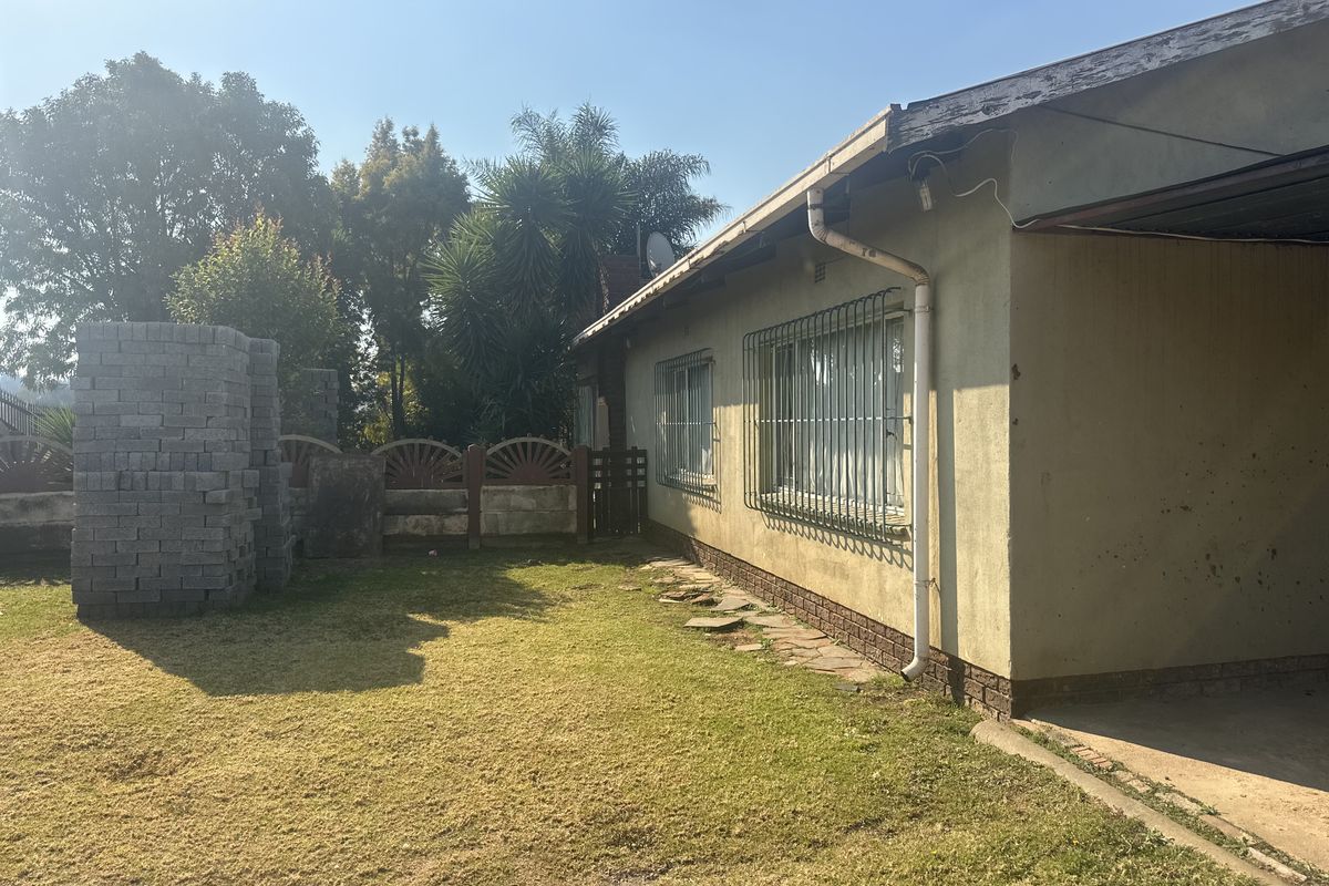 Rear exterior view of the property featuring a lawn, brick boundary wall, and security bars on the windows.