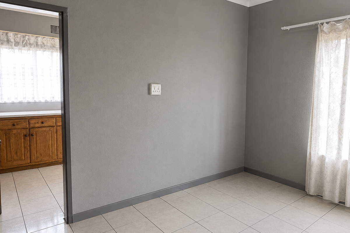 A clean, empty living area with neutral grey walls, tiled flooring, and a doorway leading into a kitchen with wooden cabinetry.