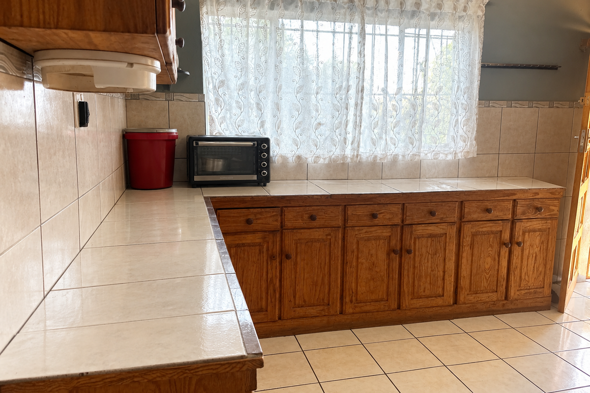 A functional kitchen featuring wooden cabinetry, tiled countertops, and tiled flooring, offering a traditional aesthetic with ample storage space.