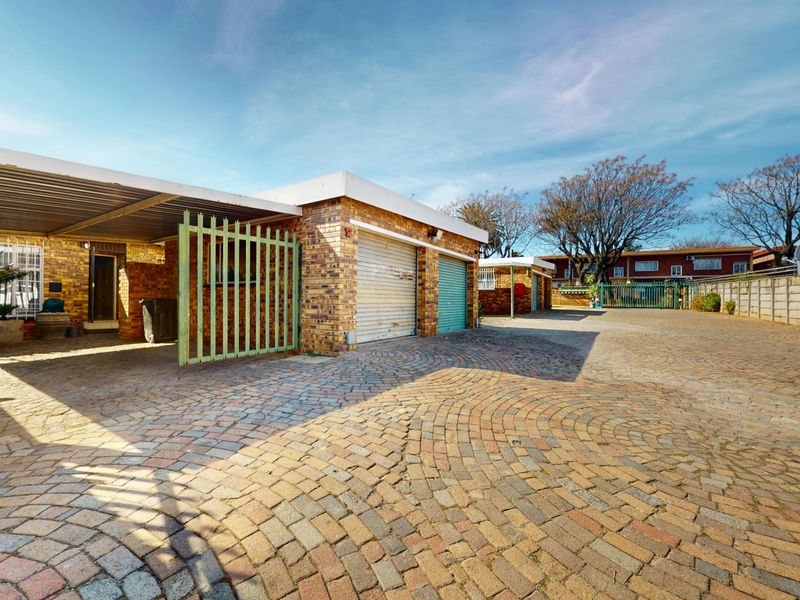 Front exterior view of the townhouse featuring a paved driveway, carport, and multiple garage doors with perimeter security walling.