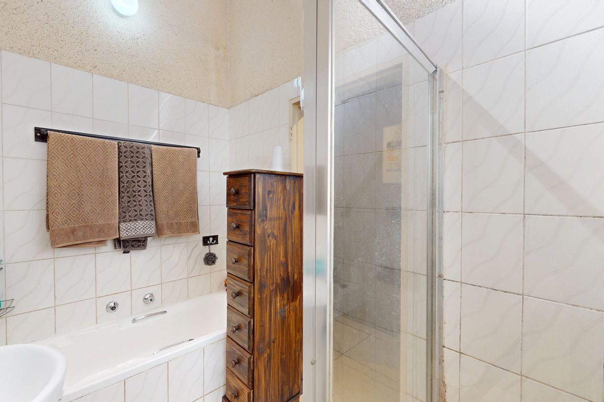 A functional bathroom featuring a built-in bathtub, separate shower enclosure, and tiled walls, offering potential for modernization and cosmetic updates.