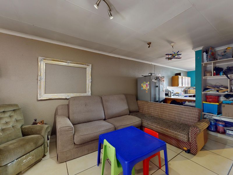Open plan living area featuring tiled flooring, built-in shelving, and ceiling spotlights, offering a functional space with potential for modernization.