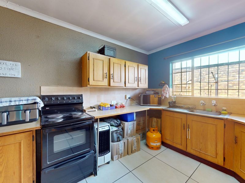 A functional kitchen featuring wooden cabinetry, a tiled backsplash, stainless steel sink, and ceramic floor tiles, offering potential for modernization.