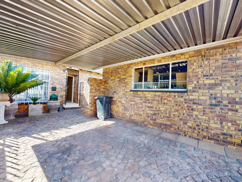 A paved front entrance area featuring a covered carport, facebrick facade, and secure gated access.
