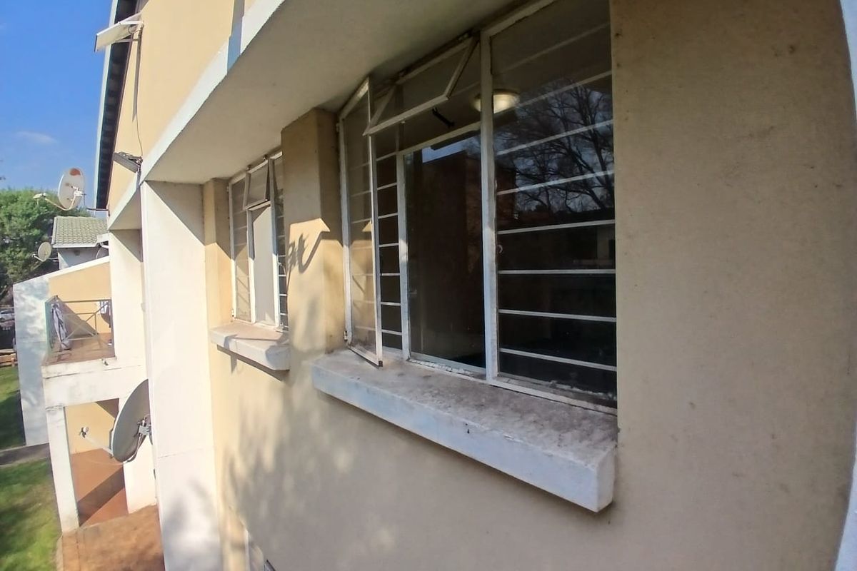 A view of the townhouse exterior rear facade featuring plastered walls, security bars on windows, and concrete sills showing signs of wear.
