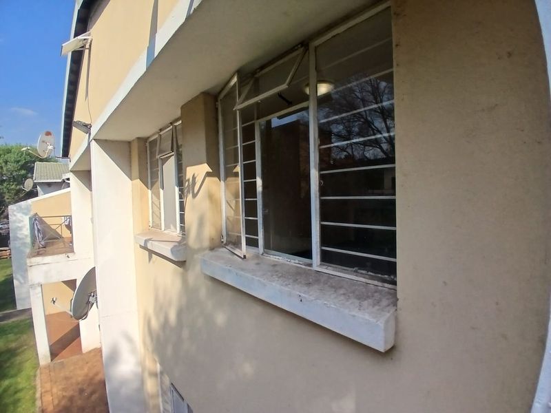 A view of the townhouse exterior rear facade featuring plastered walls, security bars on windows, and concrete sills showing signs of wear.