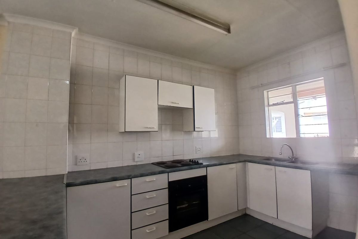 A functional kitchen featuring white built-in cabinetry, dark laminate countertops, an integrated electric hob and oven, and a double sink with tiled splashbacks.