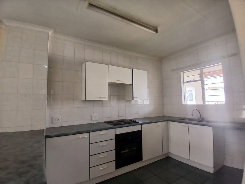 A functional kitchen featuring white built-in cabinetry, dark laminate countertops, an integrated electric hob and oven, and a double sink with tiled splashbacks.