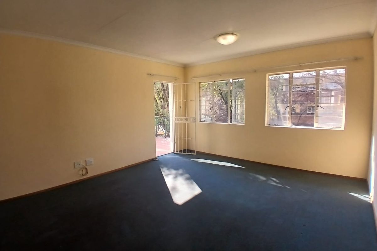 An empty, carpeted living room featuring steel-framed windows and a security gate leading to an outdoor area.