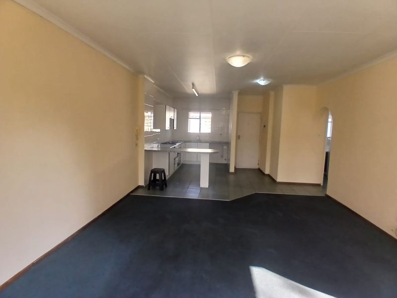 An open-plan living and kitchen area featuring a breakfast bar, built-in hob, and a combination of tiled and carpeted flooring.