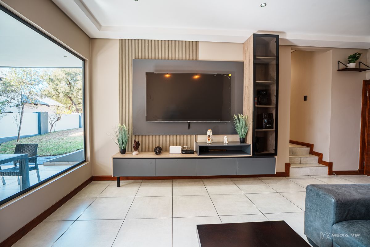 Modern living room featuring a custom built-in media unit with slatted wall detailing, large picture window, and neutral tiled flooring.