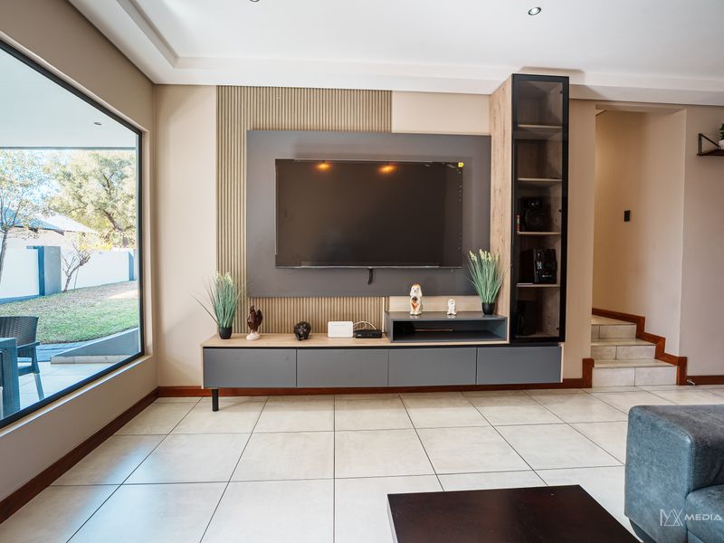 Modern living room featuring a custom built-in media unit with slatted wall detailing, large picture window, and neutral tiled flooring.