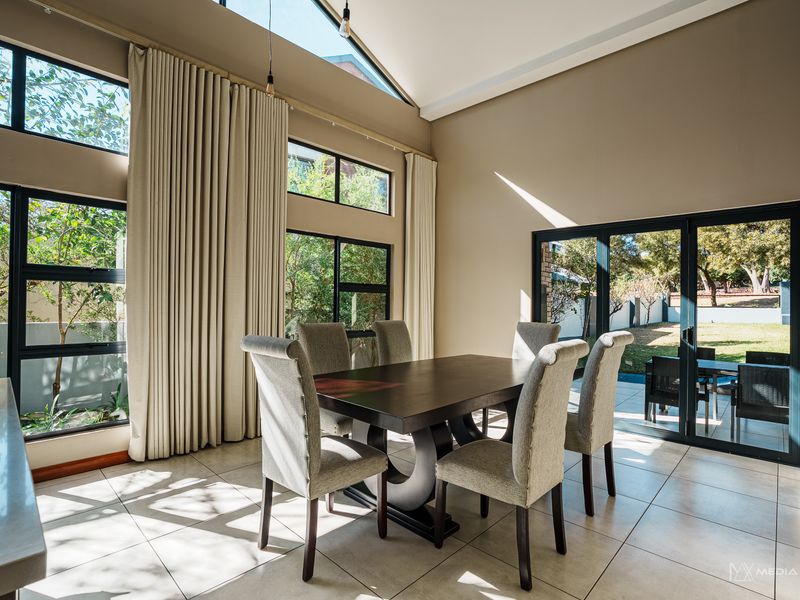 Bright dining area featuring a vaulted ceiling, large format floor tiles, and expansive windows providing natural light and views of the garden.