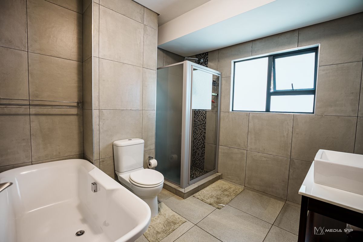 Modern bathroom featuring large format wall and floor tiles, a freestanding bathtub, a separate shower enclosure, and a vanity basin.