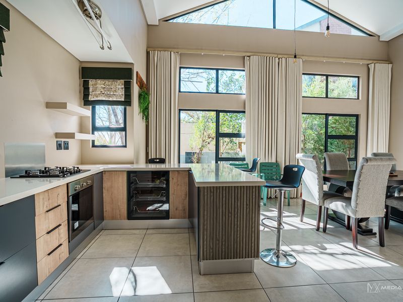 Modern open-plan kitchen and dining area featuring high-end cabinetry, integrated appliances, stone countertops, and expansive windows under a vaulted ceiling.