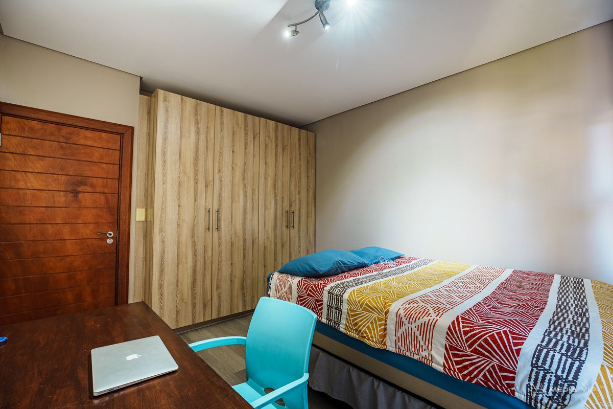 A functional bedroom featuring a large built-in wardrobe with wood-grain finish, a solid timber door, and modern track lighting.