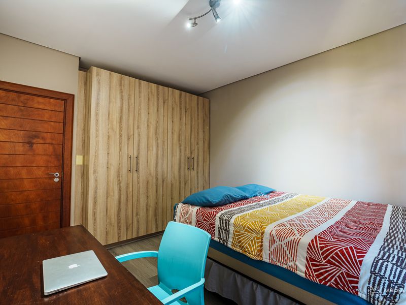 A functional bedroom featuring a large built-in wardrobe with wood-grain finish, a solid timber door, and modern track lighting.