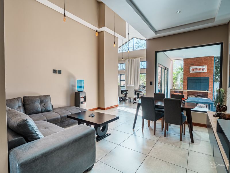Spacious open-plan living and dining area featuring high vaulted ceilings, tiled floors, and a feature brick fireplace with seamless indoor-outdoor flow.