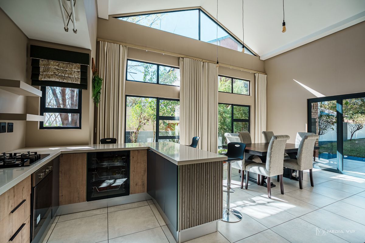 Modern open-plan kitchen and dining area featuring high vaulted ceilings, large windows, stone countertops, and integrated appliances with direct access to the patio.