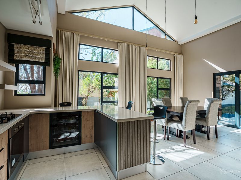 Modern open-plan kitchen and dining area featuring high vaulted ceilings, large windows, stone countertops, and integrated appliances with direct access to the patio.