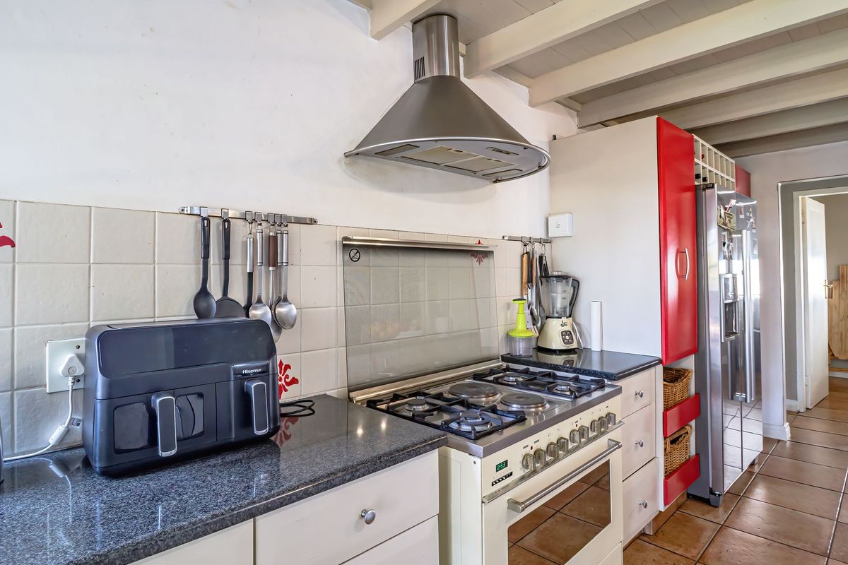 A functional kitchen featuring a gas stove, stainless steel extractor fan, granite countertops, tiled backsplash, and exposed beam ceilings.