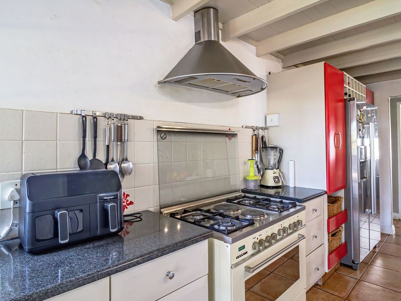 A functional kitchen featuring a gas stove, stainless steel extractor fan, granite countertops, tiled backsplash, and exposed beam ceilings.