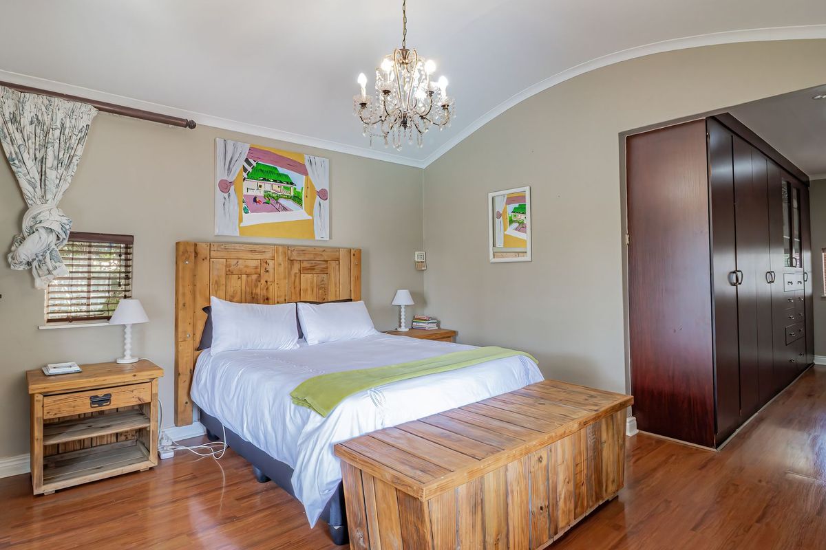 Spacious bedroom featuring hardwood flooring, built-in dark wood cupboards, and a decorative chandelier under a coved ceiling.