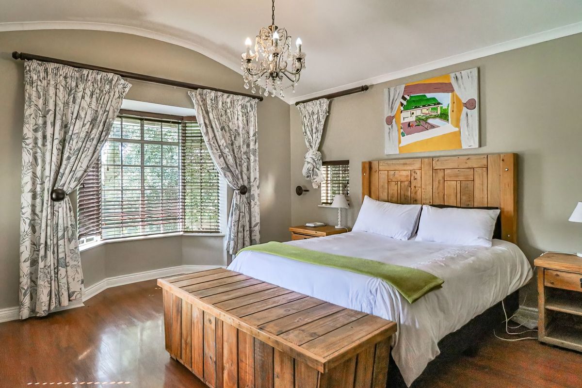 A well-maintained bedroom featuring timber flooring, a bay window, coved ceilings, and a decorative chandelier.