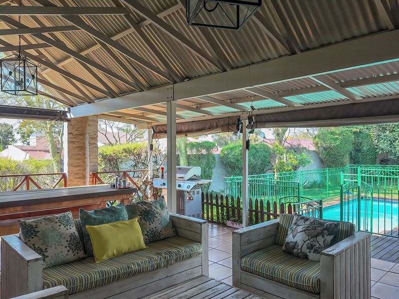 A spacious covered patio featuring tiled flooring, a timber balustrade, and direct views over the swimming pool and garden area.