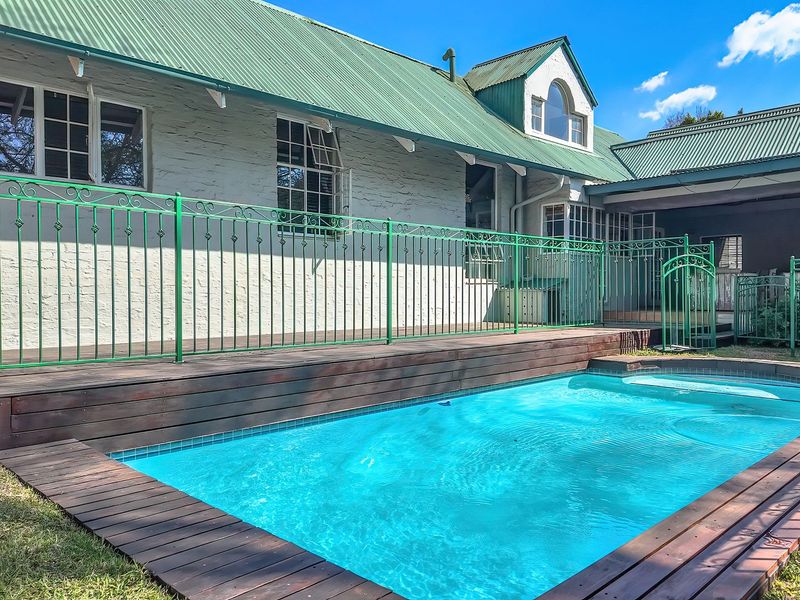 A well-maintained swimming pool area featuring timber decking, secure metal fencing, and a view of the home's exterior with a corrugated metal roof.