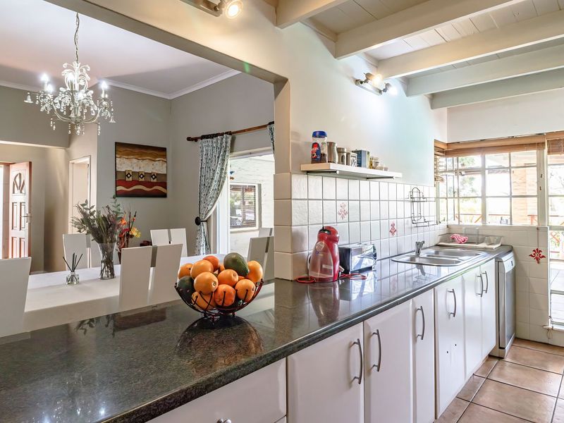 Open-plan kitchen and dining area featuring granite countertops, tiled backsplash, double basin sink, and exposed beam ceilings with a classic chandelier.