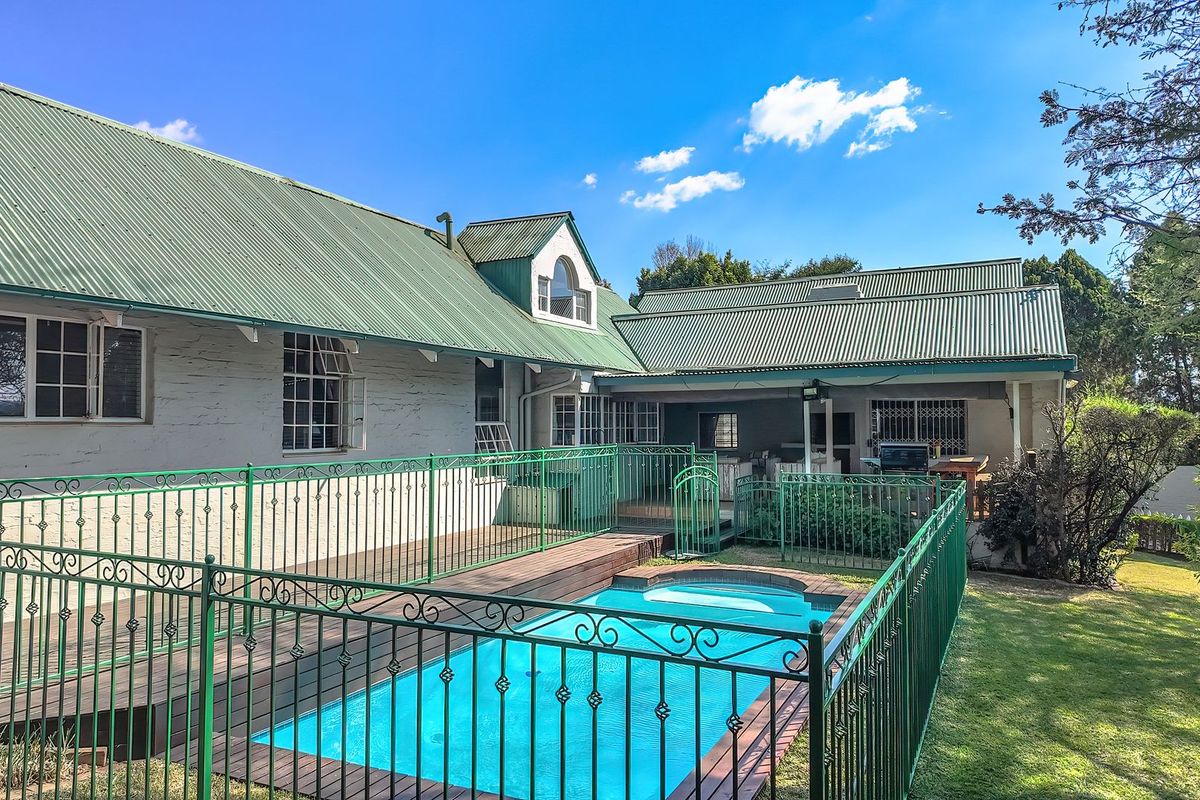 Rear exterior view featuring a swimming pool with timber decking, metal safety fencing, and a covered patio area under a corrugated metal roof.