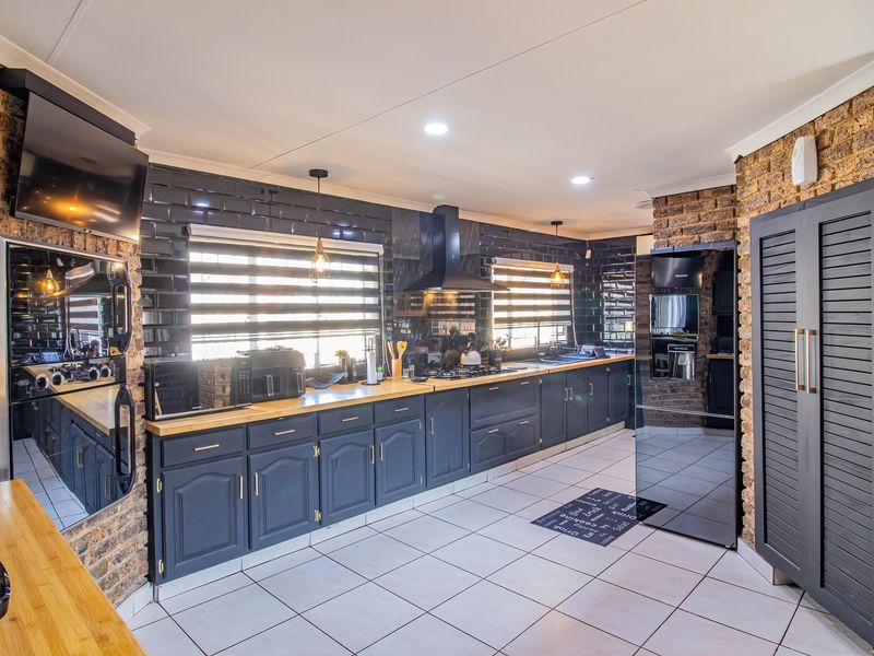 Modern kitchen featuring dark cabinetry, subway tile backsplash, exposed brick walls, wooden countertops, and high-quality built-in appliances.