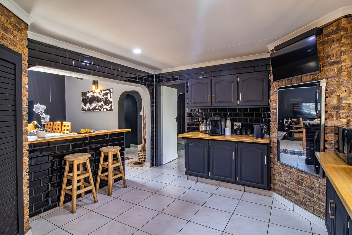 A well-maintained kitchen featuring dark cabinetry, timber countertops, subway tile backsplash, and distinctive exposed brick accents with a functional breakfast bar.