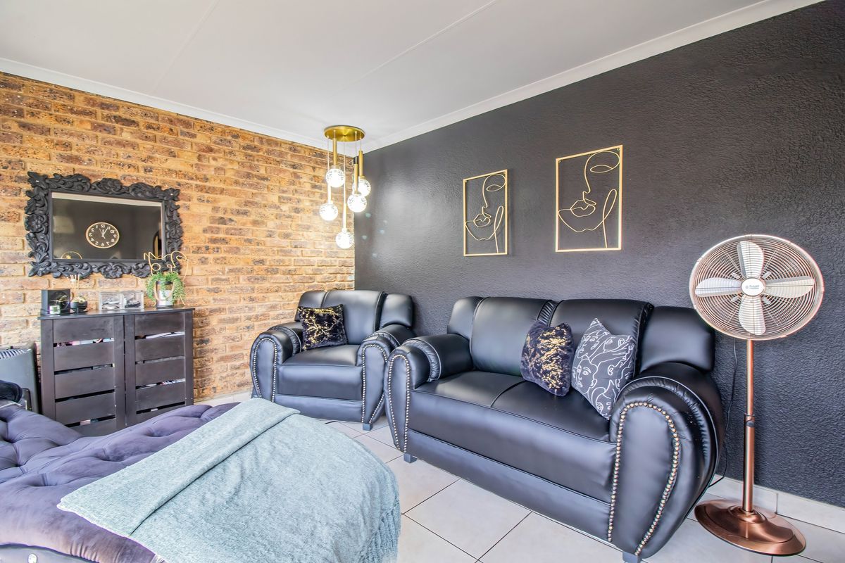 A contemporary living room featuring a striking exposed brick wall, dark accent wall, and tiled flooring, creating a stylish and modern atmosphere.