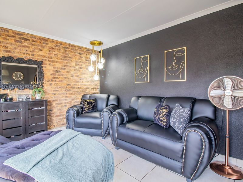 A contemporary living room featuring a striking exposed brick wall, dark accent wall, and tiled flooring, creating a stylish and modern atmosphere.