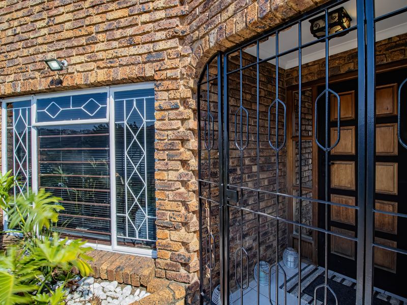 Front entrance featuring a face brick facade, secure metal gate, and a solid timber front door with decorative window security bars.