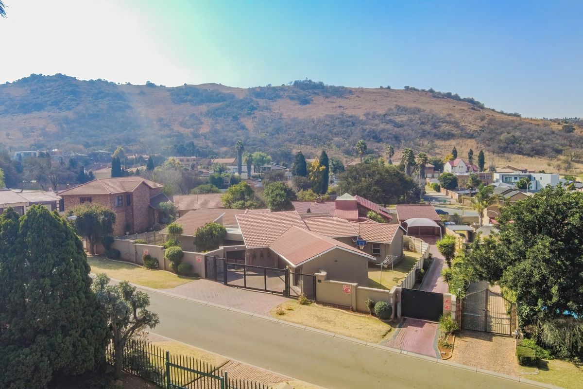 Aerial view of the property showing the main house, tiled roof, paved driveway, perimeter walling, and surrounding residential neighbourhood with mountain backdrop.