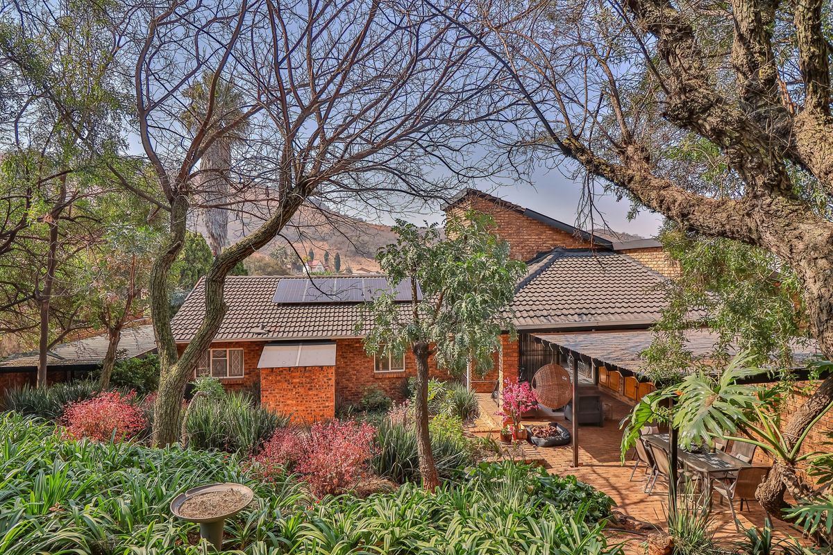 A rear view of a brick house featuring a covered patio, established garden, and roof-mounted solar panels.