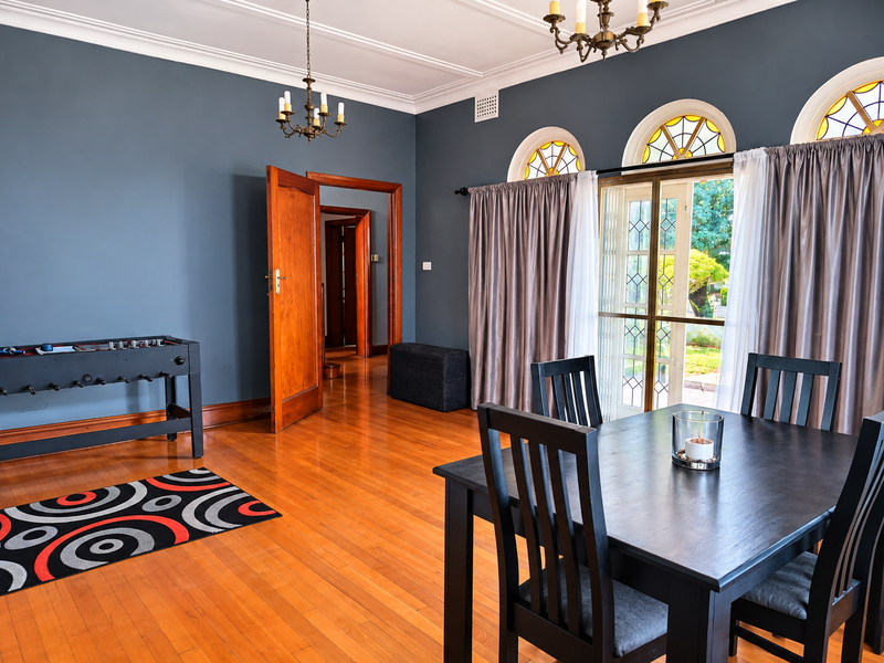 A well-maintained dining room featuring polished hardwood floors, elegant crown molding, and distinctive arched windows with stained glass accents.