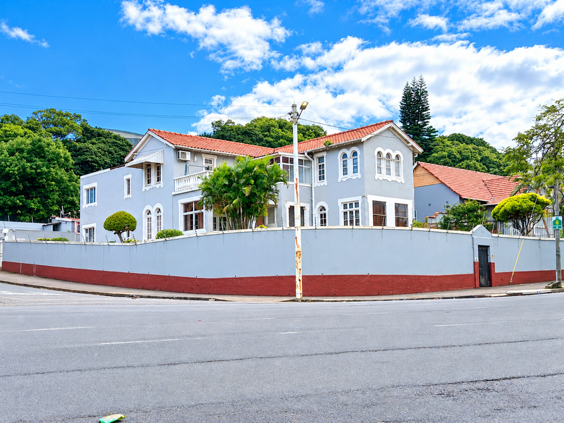 A corner-lot residential property featuring a classic architectural style with terracotta roof tiles, arched windows, and a secure perimeter wall with electric fencing.