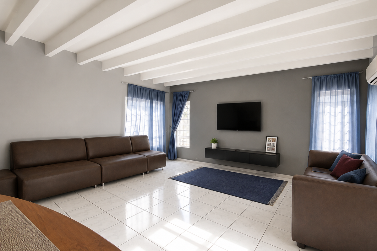 A spacious living room featuring white exposed beam ceilings, neutral grey walls, tiled flooring, and a wall-mounted floating media console.