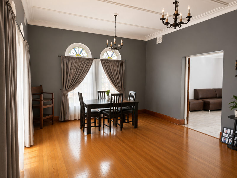 A well-maintained dining room featuring polished hardwood floors, decorative crown molding, and elegant arch windows with stained glass accents.