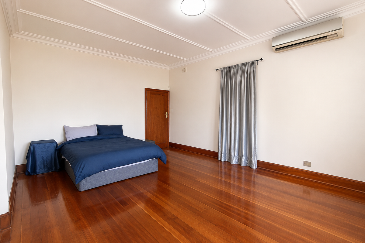 Spacious bedroom featuring polished hardwood flooring, decorative ceiling molding, and a wall-mounted split system air conditioner.