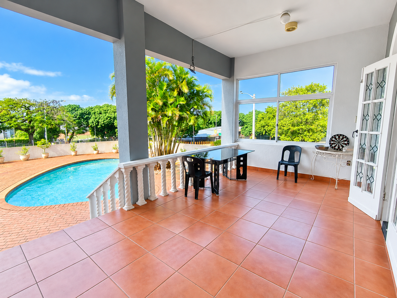 A spacious covered patio featuring terracotta tiling, overlooking a private swimming pool and garden area, ideal for outdoor entertaining.