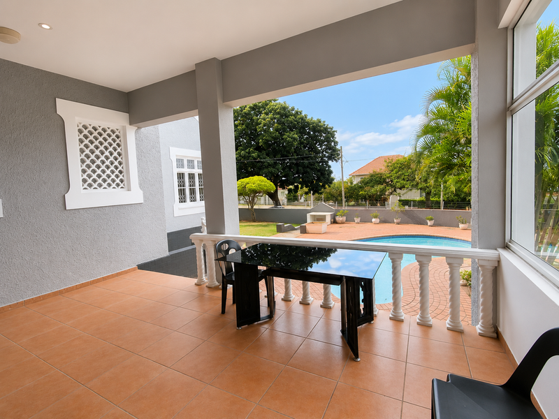 Covered patio area featuring tiled flooring, a decorative balustrade, and direct views overlooking the swimming pool and garden.